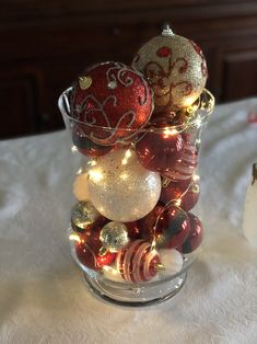 a glass vase filled with christmas ornaments on top of a white tablecloth covered table