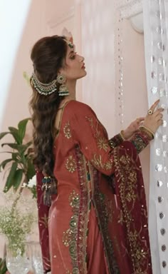 a woman in a red dress standing next to a window with beaded trims