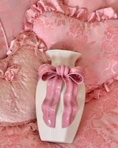 a pink and white vase sitting on top of a bed next to two pillow cases