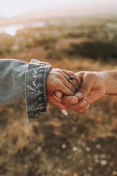 two people holding hands while standing on top of a field