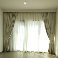 an empty living room with large windows and drapes