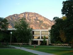 a building with mountains in the background and trees on the sidewalk leading up to it