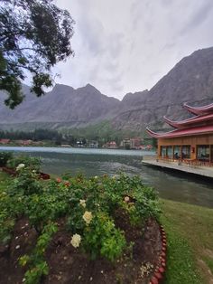 a building sitting on top of a lush green hillside next to a lake and mountains