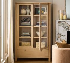 a wooden cabinet with glass doors and shelves in a living room next to a window