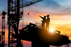 two people are standing on top of a building under construction at sunset or dawn with the sun setting behind them