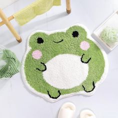 a green frog rug sitting on top of a white floor next to shoes and towels