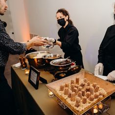 three people in masks are serving food to each other at a buffet table with candles on it