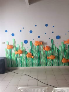 some orange fish are swimming in the water near green grass and blue bubbles on the wall