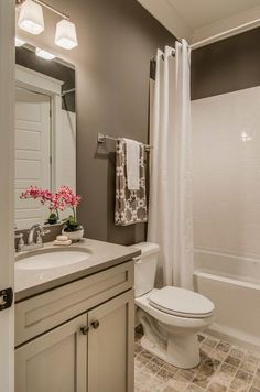 a white toilet sitting next to a bath tub under a bathroom mirror with lights on