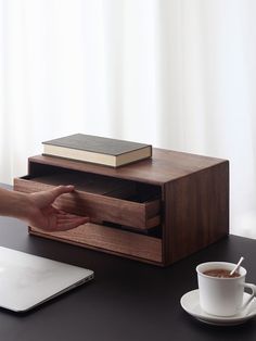 a person's hand reaching into an open drawer on a desk next to a laptop