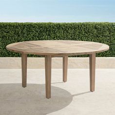 a wooden table sitting on top of a cement floor next to a green hedge covered wall