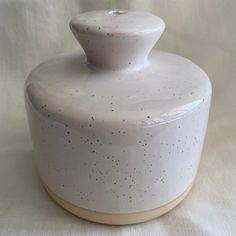 a white ceramic jar with speckles on the top and bottom, sitting on a white surface