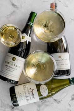 three bottles of wine and two empty glasses on a marble counter top with one bottle in the middle