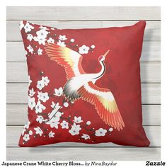 a red pillow with an image of a crane on it and white flowers in the background