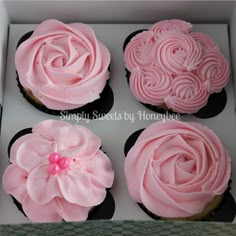 four cupcakes with pink frosting and flowers on top are in a box