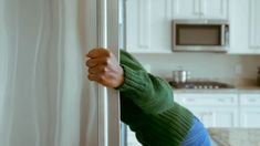 a woman in green sweater holding on to a white refrigerator door with her hand over the handle