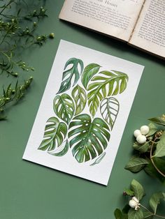 an open book sitting on top of a green table next to plants and other items