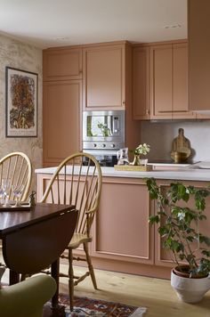 a kitchen with pink cabinets and wooden chairs next to a dining table in front of an oven