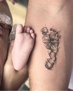 a person with a tattoo on their arm holding a baby's foot and looking at the camera