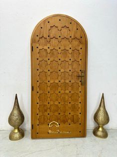 an ornate wooden door with two gold vases next to it on a white wall