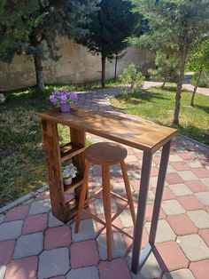 a wooden table with two stools in the middle of a brick walkway next to trees