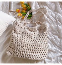 a white crocheted bag sitting on top of a bed next to a book