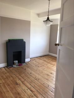 an empty room with wood flooring and a fireplace in the corner, next to a door