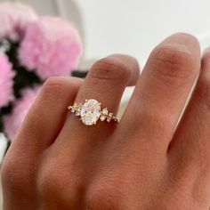 a woman's hand with a diamond ring on top of her finger and pink flowers in the background