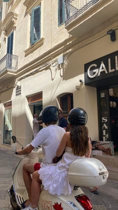 a man and woman riding on the back of a scooter down a street