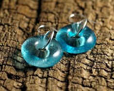 two blue earrings sitting on top of a piece of wood