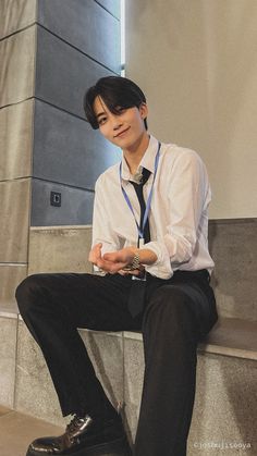 a young man sitting on top of a cement bench wearing a tie and holding a cell phone