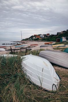 there are several boats on the beach and one is upside down in the grass by the water