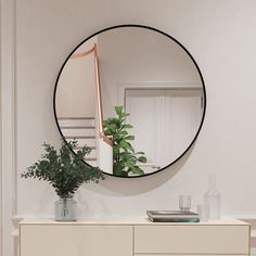 a round mirror hanging on the side of a wall above a dresser with a potted plant