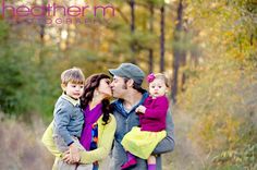 a man, woman and two children are kissing in the woods