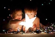 two young boys are playing with a star in the dark, surrounded by christmas lights