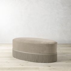 a round ottoman sitting on top of a hard wood floor next to a white wall