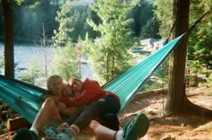 two people are laying in a hammock by the water