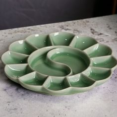 a green bowl sitting on top of a counter next to a white plate with a spiral design