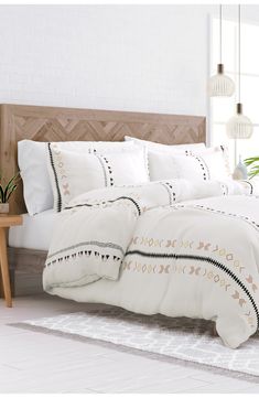 a bed with white comforter and pillows in a room next to a plant on the floor