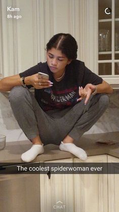 a woman sitting on top of a kitchen counter looking at her cell phone