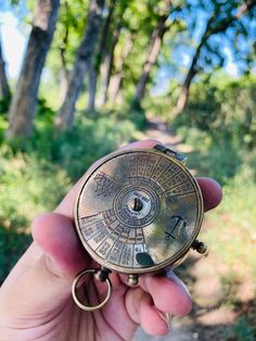 a person holding an old pocket watch in their left hand with trees in the background