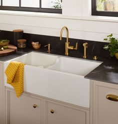 a white kitchen sink sitting under a window next to a counter top with gold faucets