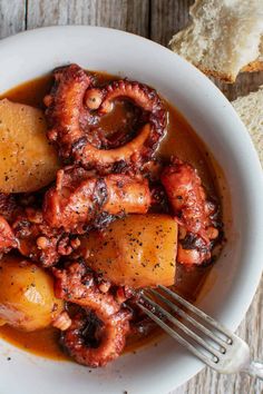 octopus stew in a white bowl with bread on the side and a fork stuck into it