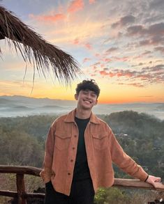 a man standing on top of a wooden balcony next to a lush green forest covered hillside