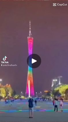 people are standing around in front of a tall building with a rainbow light on it