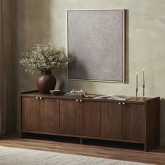 a vase with some flowers on top of it next to a wooden cabinet and mirror