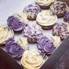 cupcakes with white and purple frosting are arranged in a box on a table