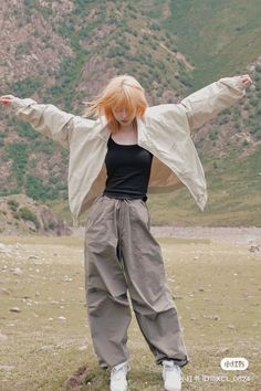 a woman standing in the grass with her arms spread out and hands outstretched, wearing an overstuffed jacket