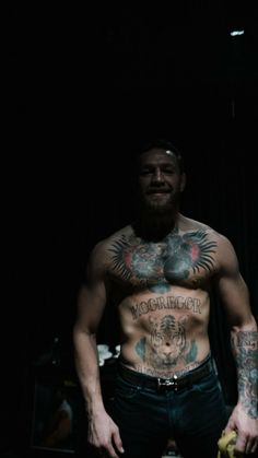 a shirtless man with tattoos on his chest stands in front of a black background