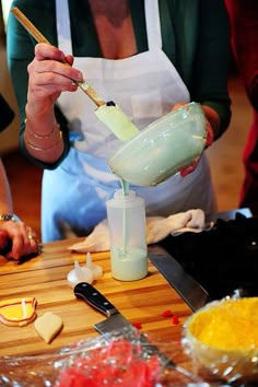 a person pouring something into a blender on top of a wooden table with other items